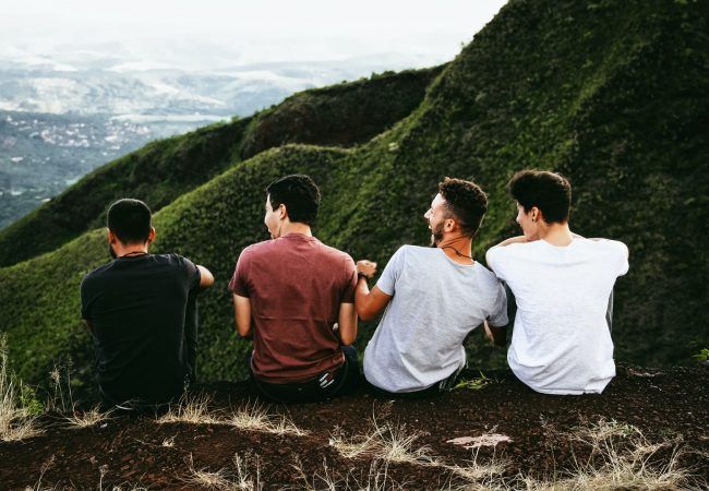 row of four men sitting on mountain trail