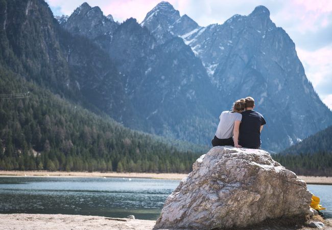 a couple sits on a rock looking out over a lake